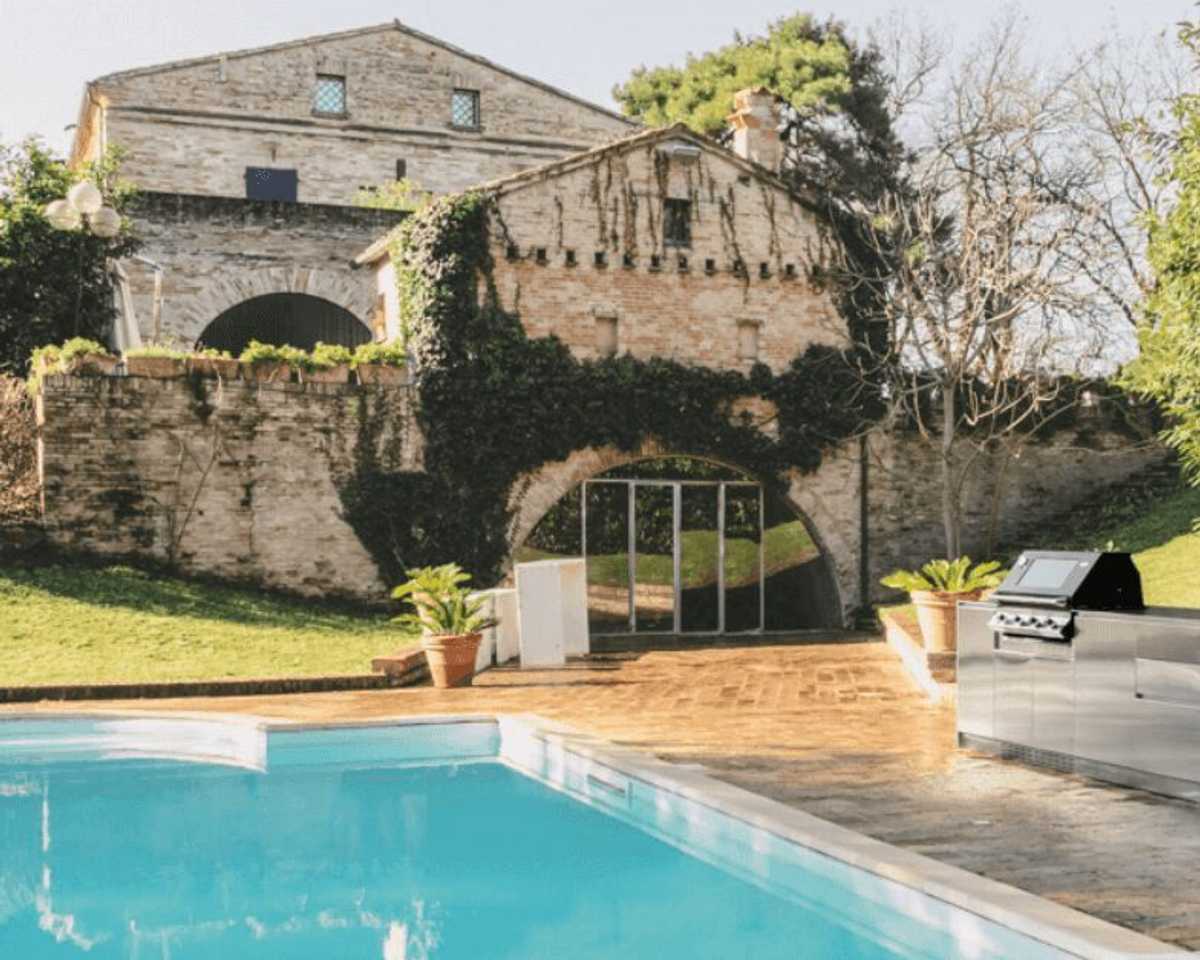 Stainless steel Italian outdoor kitchen beside a pool with stone architecture in the background.